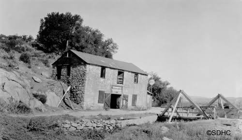 The stone Gaskill Brothers Store rebuilt after the 1916 flood, with a wooden bridge alongside